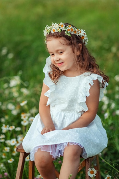 Portrait of a little cheerful girl with a wreath of daisies on her head