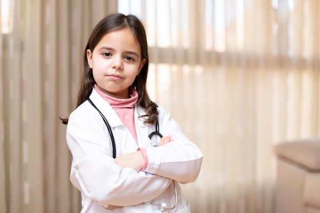 Portrait of little child in doctor's uniform posing with crossed arms and responsible attitude