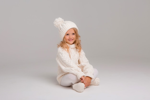 Portrait of a little curly-haired girl in a knitted white winter hat