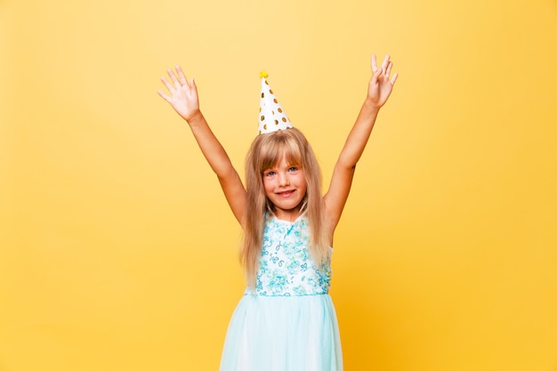 Portrait of a little cute girl in a festive cap on a yellow background. Birthday, holiday.