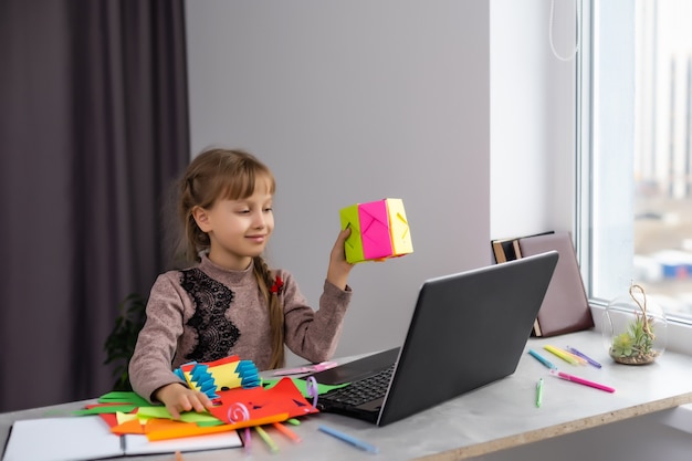 Portrait of little girl cutting a paper make art craft activities stay at home from Coronavirus covid-19 crisis. Child cutting paper with scissors online learning. homeschooling kid.