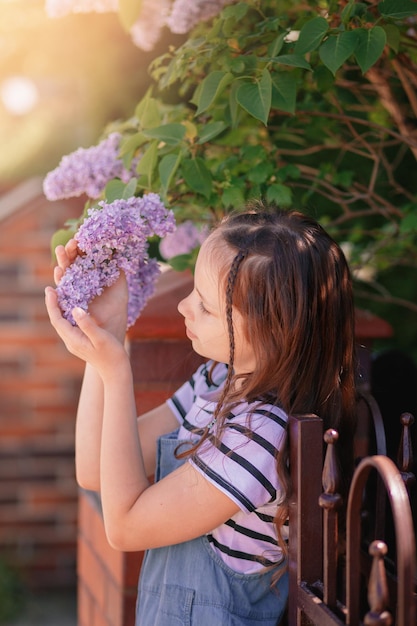 Portrait of little girl holding blossoming liliac flowers Adorable kid child outdoors on warm spring day Vertical