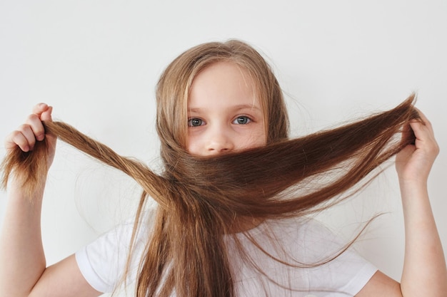 Portrait of little girl holding hair in hands on white background