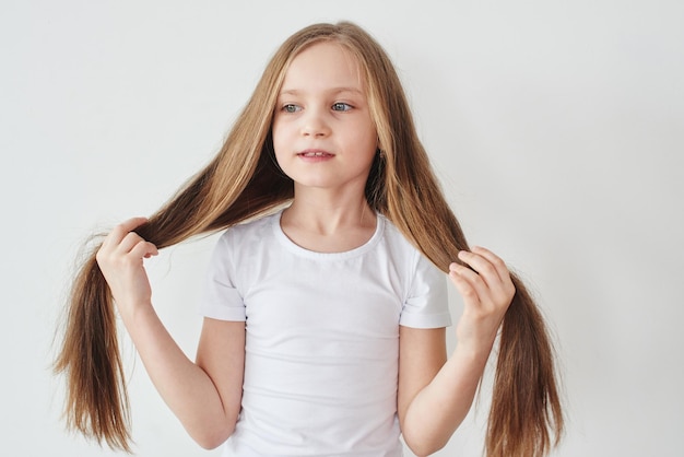 Portrait of little girl holding hair in hands on white background