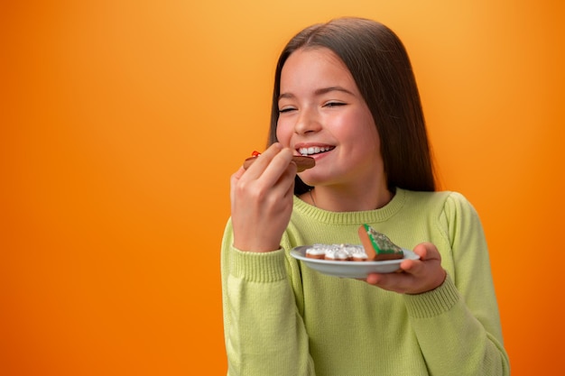 Portrait of little girl holding plate with cookies against orange background