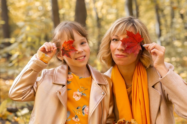 Portrait of a little girl and mother She covers her eye with a maple autumn leaf Fall season and children concept