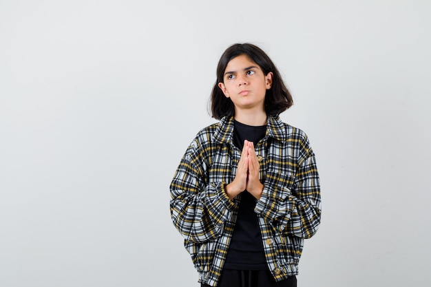 Portrait of little girl showing clasped hands in pleading gesture in t-shirt, jacket and looking hopeful front view