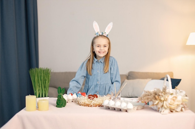 Portrait of little girl standing in modern light kitchen and paining Easter eggs