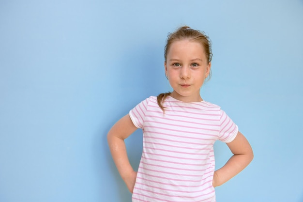 Portrait of a little girl with a businesslike pickystrict look hands on her belt on a blue background with copy space