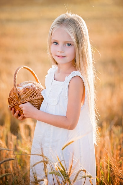 Portrait of a little girl with long blond hair in a white dress standing in a field among the ears of wheat