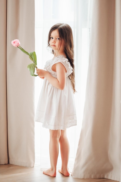 Portrait of a little girl with long dark hair closeup The baby hugs a bouquet of fresh delicate pink tulips A gift for the holiday spring time