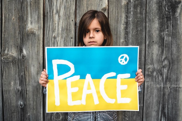 Portrait of the little girl with the Ukrainian flag placard and the inscription PEACE Solidarity with Ukrainian children and people who are currently at war Concept of war in Ukraine