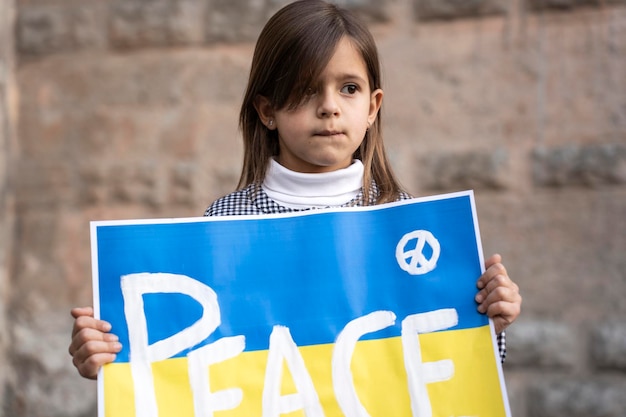 Portrait of the little girl with the Ukrainian flag placard and the inscription PEACE Solidarity with Ukrainian children and people who are currently at war Concept of war in Ukraine