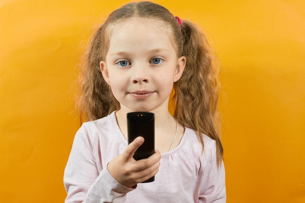 Portrait of a little girl on a yellow background holding a remote control from the TV.