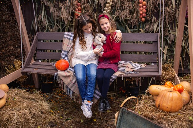 portrait of little girls girlfriends in the fall with a rabbit in their hands near their house fam