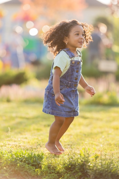 Portrait little happy playful swarthy girl in a denim sundress standing in the garden on a sunny day