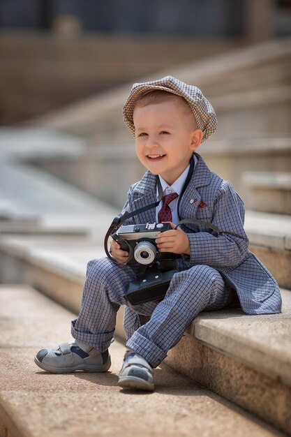 Photo portrait of a little kid boy photographer taking picture with retro vintage photo camera on the steps outside children's photo shoot people childhood lifestyle concept