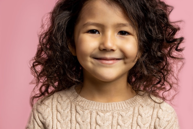 portrait of little kid girl 5 y.o. with dark curly hair, brown skin, charming smile, brown eyes, wearing beige sweater, smiling looking.