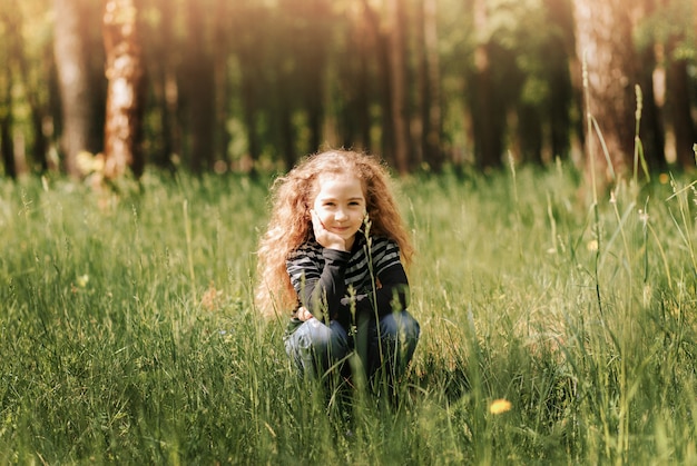 Portrait of a little laughing girl against a background of grass in the park in summer. Happy childhood.