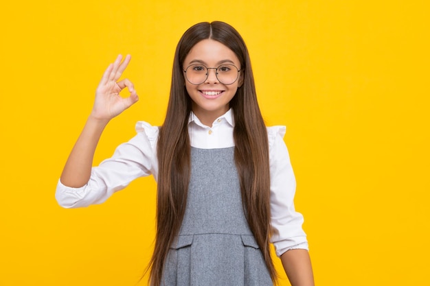 Portrait of a little teenager child girl showing okay gesture isolated over yellow background Ok sign concept Happy girl face positive and smiling emotions