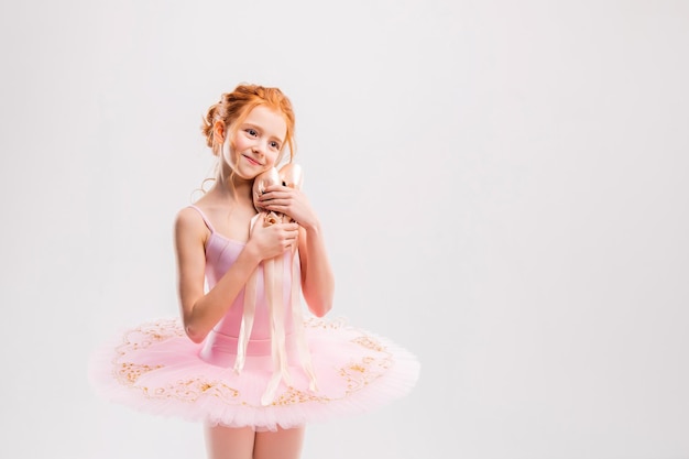 Portrait of a little tender redhaired girl in a pink tutu with pointe shoes dreaming of becoming a ballerina