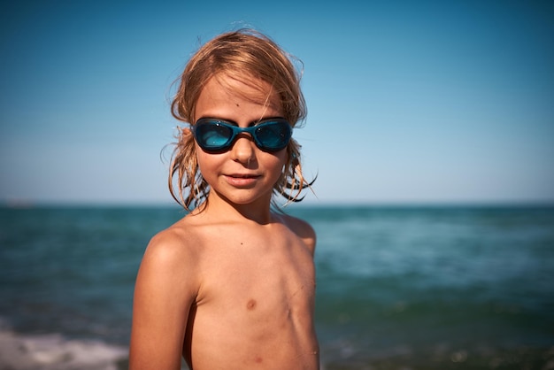 Portrait of a longhaired 8 year old boy in swimming goggles against the backdrop of the sea on a on a summer evening