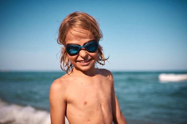 Portrait of a longhaired 8 year old boy in swimming goggles against the backdrop of the sea on a on a summer evening