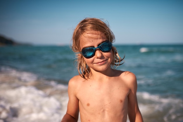 Portrait of a longhaired 8 year old boy in swimming goggles against the backdrop of the sea on a on a summer evening