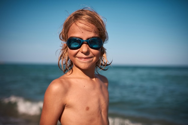 Portrait of a longhaired 8 year old boy in swimming goggles against the backdrop of the sea on a on a summer evening