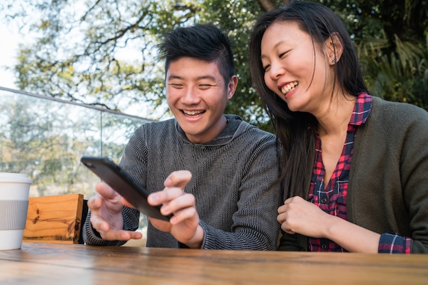 Portrait of lovely asian couple looking at the mobile phone while sitting and spending time at the coffee shop. Love and technology concept.