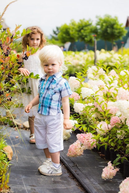 Portrait of lovely blonde boy with long hair posing outdoors near bushes with black berries Curious toddler at botanical garden Kid discovering nature