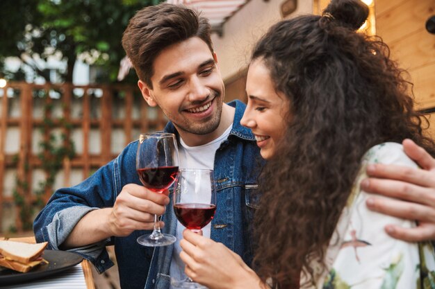 Portrait of lovely couple man and woman drinking red wine while hugging together near trailer outdoors