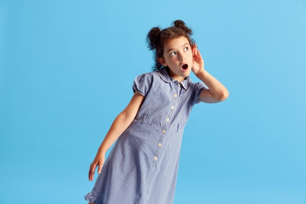 Portrait of lovely little girl child with curly hair and cute hairdo posing against blue studio