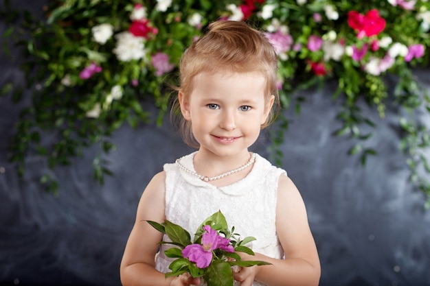 Portrait of the lovely little girl with a bouquet of flowers. Looking at camera