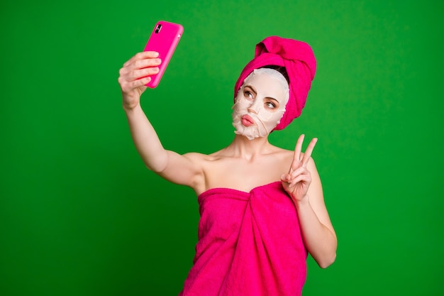 Portrait of lovely pretty lady wearing turban using facial mask taking selfie showing v-sign pout lips isolated on bright green color background