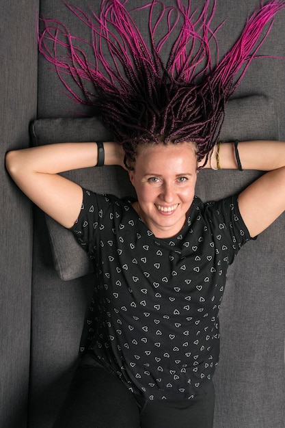 Portrait of lovely smiling caucasian woman with pink dreadlocks on sofa Youth lifestyle and trendy people concept