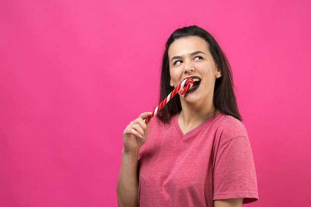 Portrait of lovely sweet beautiful cheerful woman with straight brown hair trying to bite red candy cane christmas.