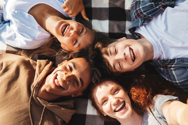 Portrait of lovely young friends guys and girls laughing, and lying on blanket in circle outdoor