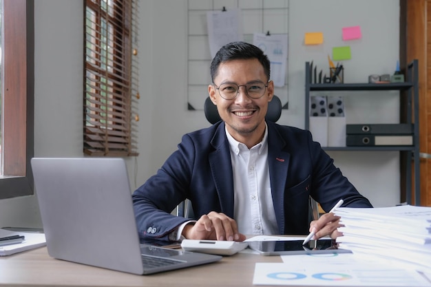 Portrait of a male business owner showing a happy smiling face as he has successfully invested his business using computers and financial budget documents at work