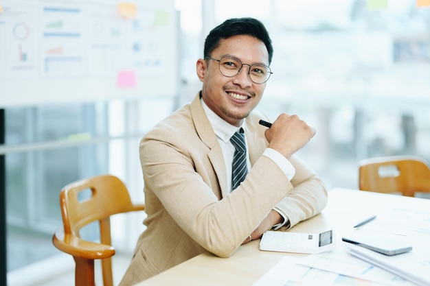 Portrait of a male business owner showing a happy smiling face as he has successfully invested his business using computers and financial budget documents at work