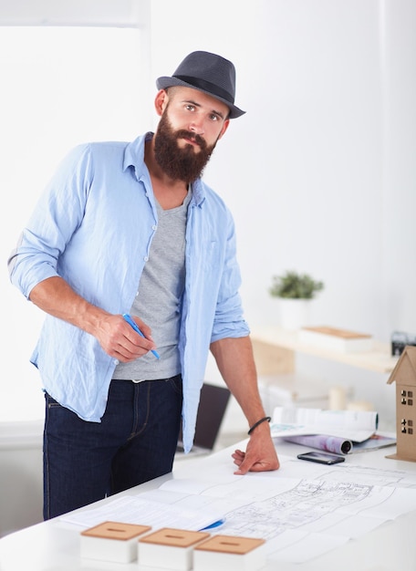 Photo portrait of male designer with blueprints at desk in office.