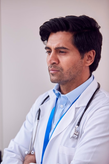 Portrait Of Male Doctor Or GP with Stethoscope Wearing White Coat Standing In Office