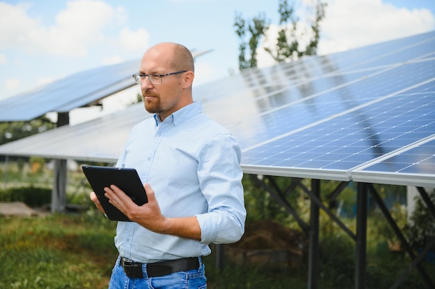 Portrait of male engineer with tablet in his hands near the solar panels station wearing helmet at sunny day Green ecological power energy generation