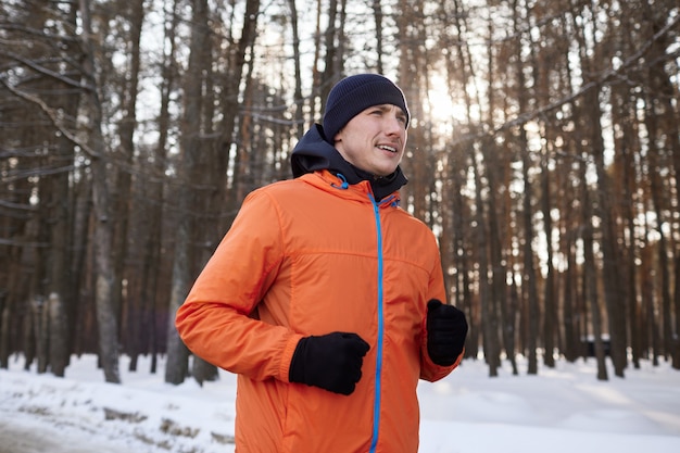 Portrait of a man in bright sports clothes running through a winter forest. Frosty day