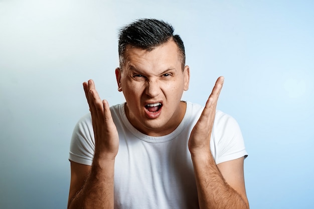 Portrait of a man close-up, experiencing anger, hate, against a light background.