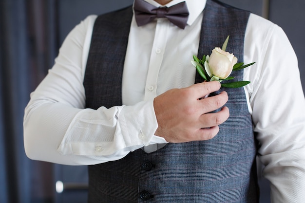 Portrait man in dark suit and white shirt corrects boutonniere close up grooms hand with buttonhole