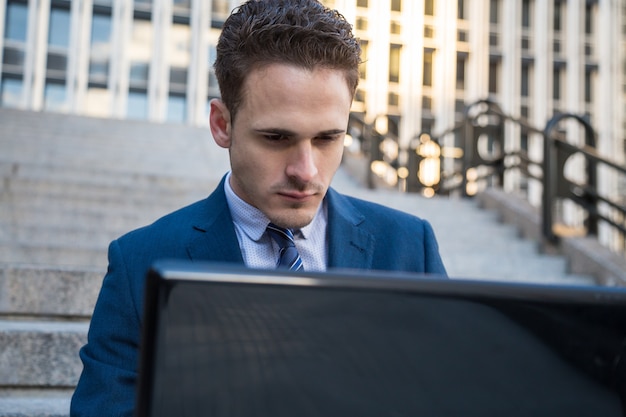 Portrait of man in elegant suit working on stairs with laptop on knees. 