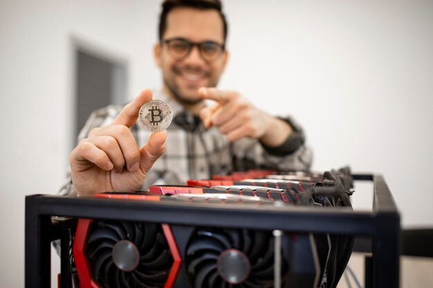 Portrait of man expert programmer holding bitcoin and standing by cryptocurrency mining rig