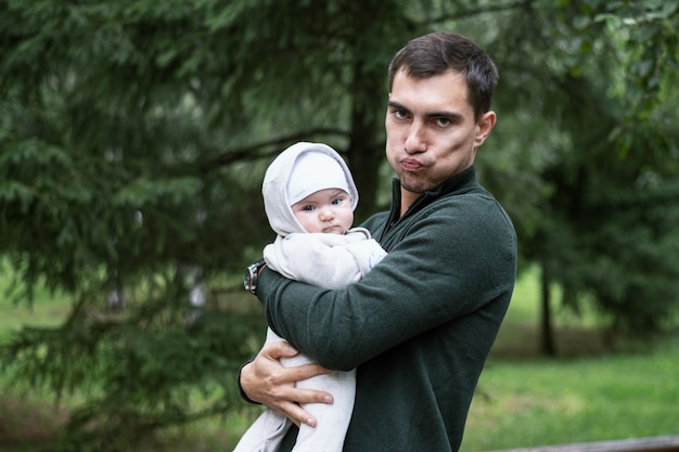 Portrait of man in green jacket making faces with child in his arms in Park in fresh air, walking with child concept