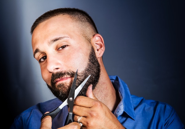 Portrait of a man grooming his beard with scissors